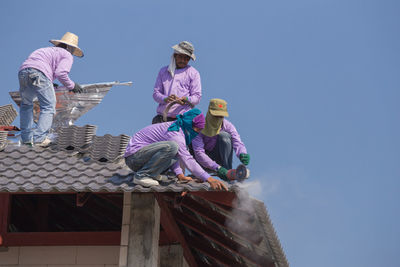 Low angle view of people working against clear blue sky