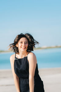 Portrait of smiling young woman standing by sea against sky