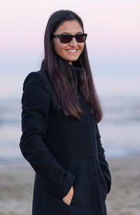 Beautiful young woman standing at beach during sunset