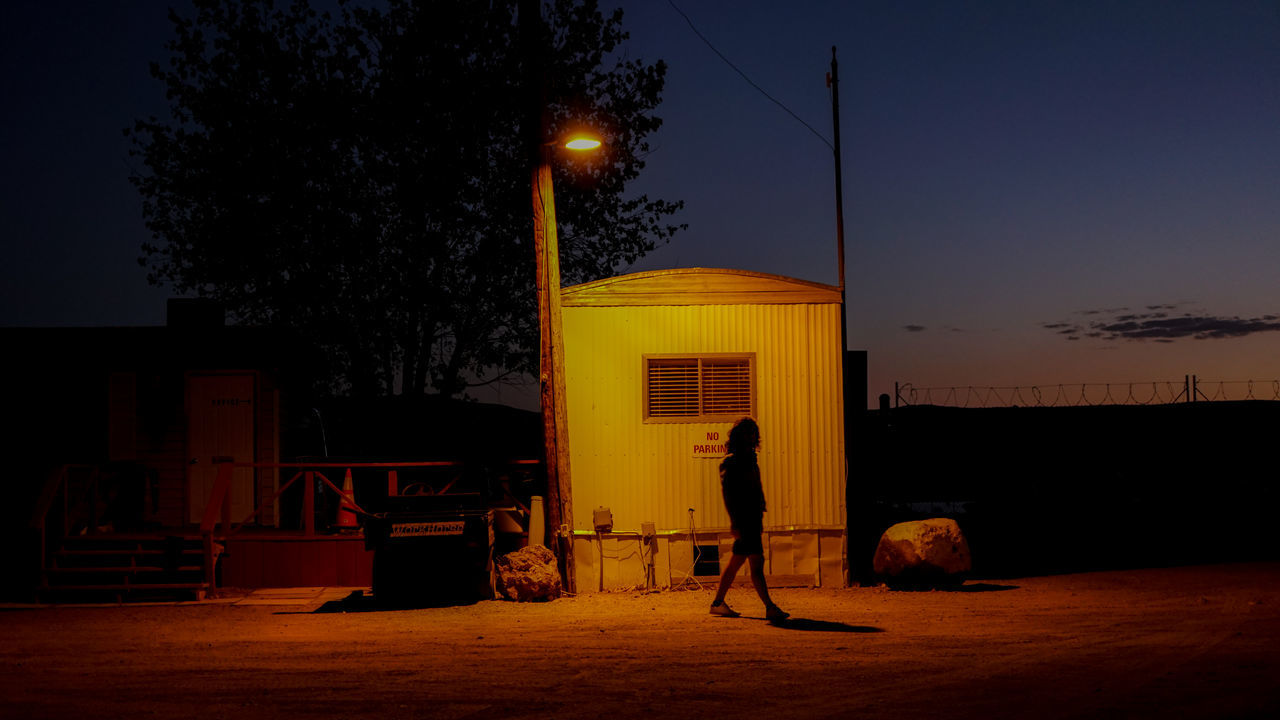 SILHOUETTE MAN ON ILLUMINATED STREET AGAINST ORANGE SKY