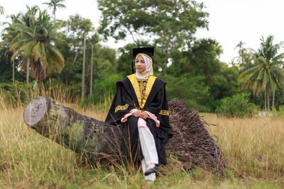 Woman in graduation gown sitting on log