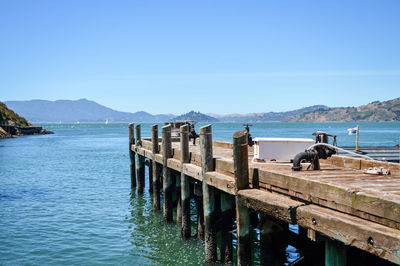 Wooden posts in sea against clear blue sky