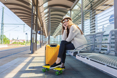 Teenage girl wearing sunglasses sitting at railroad station platform