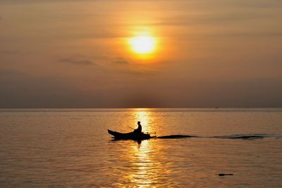 Silhouette man in sea against sky during sunset