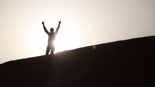 Silhouette of woman with arms raised against sky during sunset