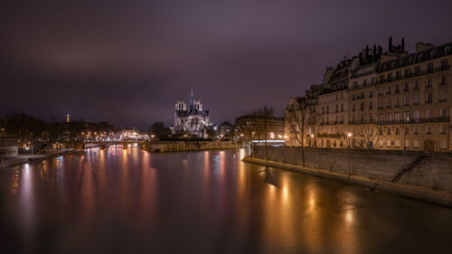 Illuminated buildings by river against sky at night