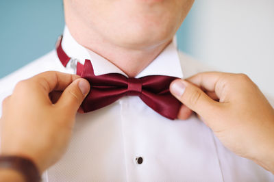 Friend helping bridegroom while wearing bow tie during wedding