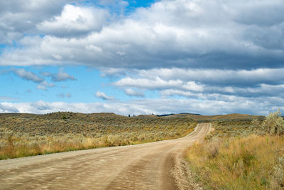 Empty road amidst field against sky