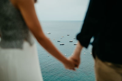 Midsection of couple holding hands against sea