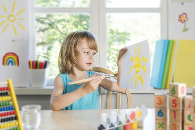 Boy painting while sitting by table