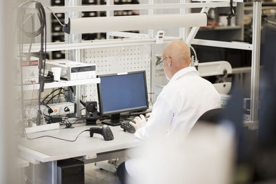 Rear view of mature engineer using computer in manufacturing plant