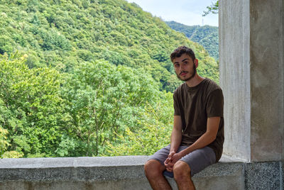 A relaxed boy, sitting on a low wall, looks towards the camera