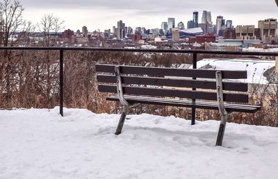Empty bench against cityscape during winter
