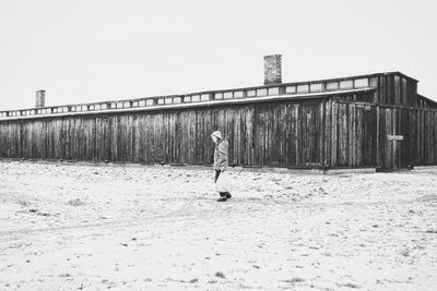 Person walking on snow covered landscape with house in background