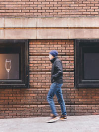 Side view of man walking against brick wall