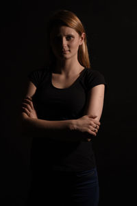 Portrait of young woman standing with arms crossed against black background