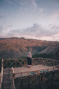 Rear view of woman standing by railing against sky