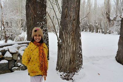 Portrait of smiling girl standing on snow covered tree
