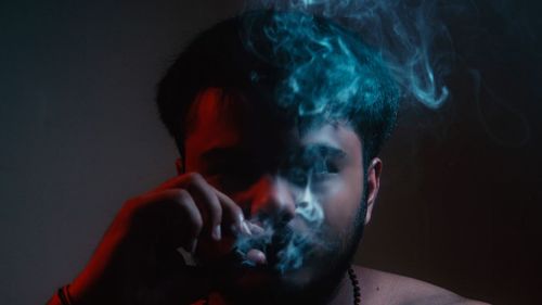 Portrait of man smoking against black background