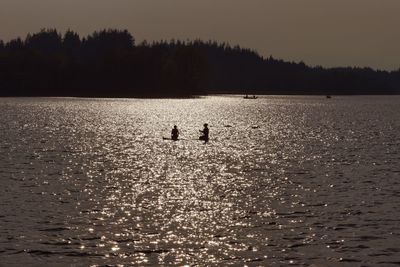 Silhouette people swimming in lake against sky