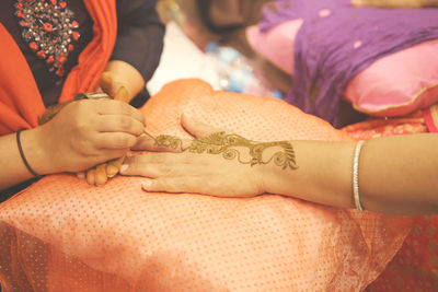 Midsection of woman making henna tattoo on friend hand 