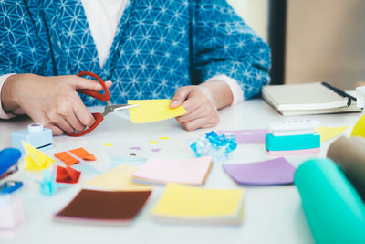 Midsection of woman making paper craft while sitting on table at home