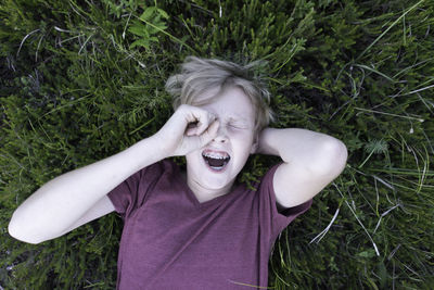 High angle view of playful teenage boy relaxing on grassy field