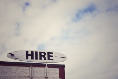 Close-up of hire signboard against clouds