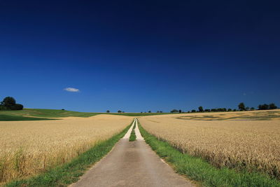 Road amidst field against clear blue sky