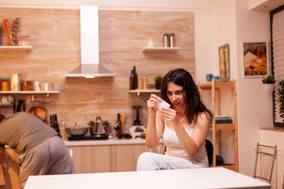 Portrait of young woman using mobile phone while sitting at home
