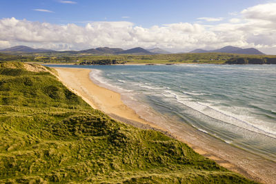 Scenic view of landscape and beach against cloudy sky