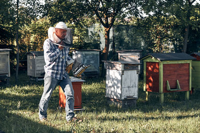 Beekeeper holding smoker while walking in yard 