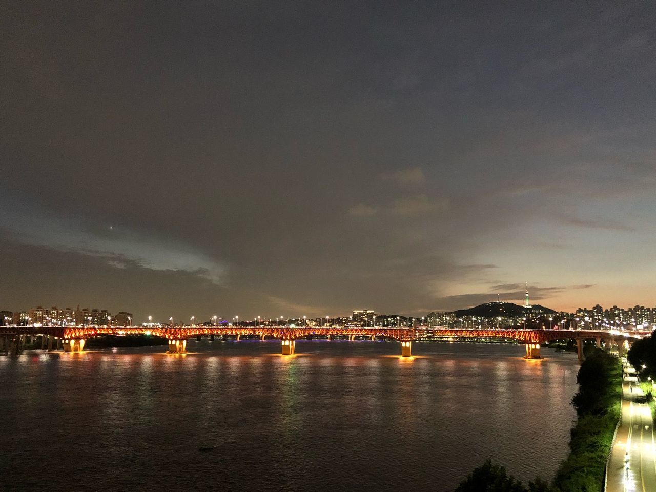 ILLUMINATED CITY BY RIVER AGAINST SKY