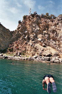Man on rock by sea against sky