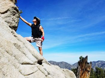 Low angle view of mature man climbing on rocky mountain against blue sky