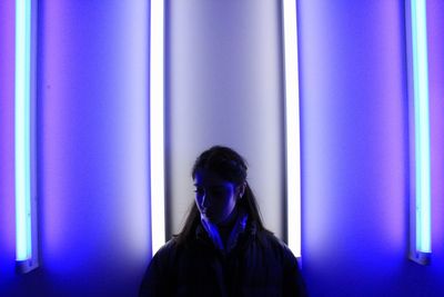 Portrait of young woman standing against blue wall