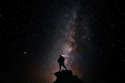 Silhouette person standing on rock against star field at night