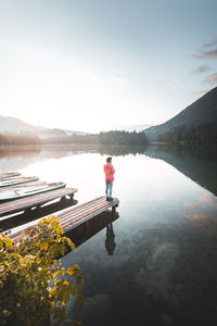 Woman standing on pier over lake against sky