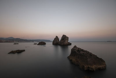 Rocks on sea against clear sky during sunset