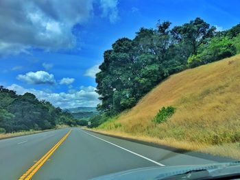 Mountain road amidst trees against sky seen through car windshield