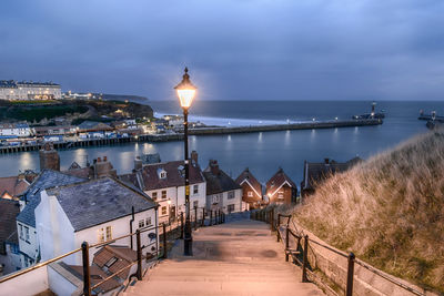 Illuminated pier by sea against sky at dusk