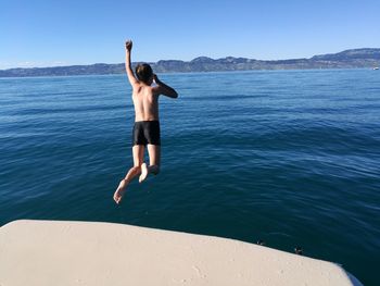 Full length of shirtless boy jumping in sea against clear sky