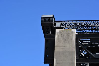 Low angle view of bridge against building against clear blue sky