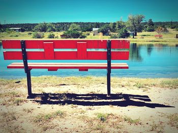 Red bench by lake against clear sky