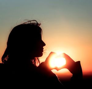 Silhouette woman making heart shape against sun