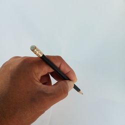 Close-up of hand holding pencil against white background