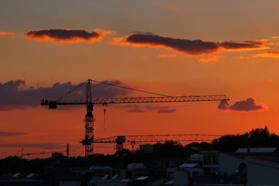 Silhouette cranes at construction site against sky during sunset