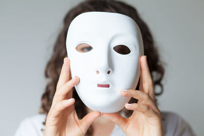 Close-up portrait of woman holding mask against white background