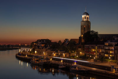 Illuminated buildings by river against sky at night