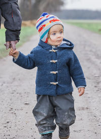 Cute girl holding cropped father hand while standing on road